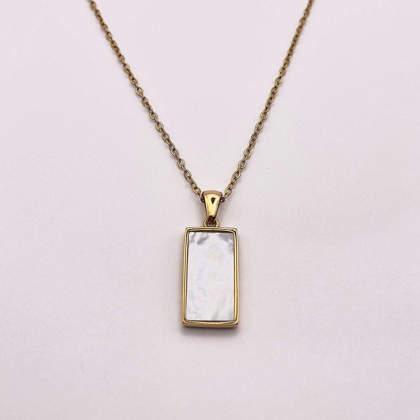 Back view of an enchanting gold plated necklace perfected with a rectangular tarot card, the Wheel (-X-), sculpted with stunning gold plated artistry, detailed with white zircons, and white pearl colored stone backed.