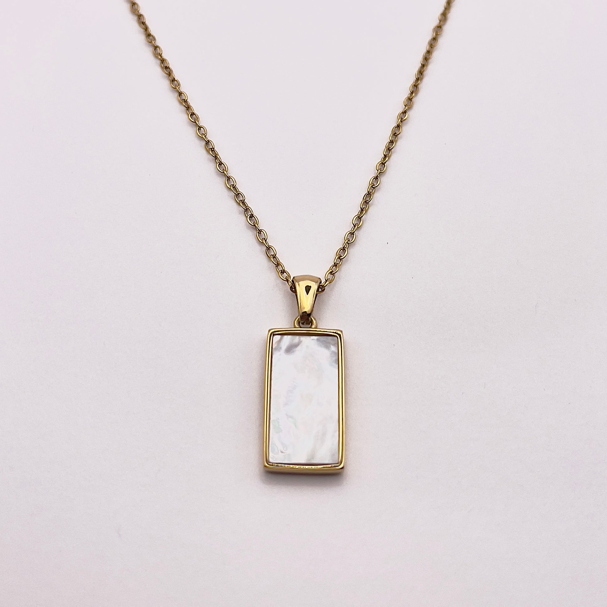 Back view of an enchanting gold plated necklace perfected with a rectangular tarot card, the Wheel (-X-), sculpted with stunning gold plated artistry, detailed with white zircons, and white pearl colored stone backed.