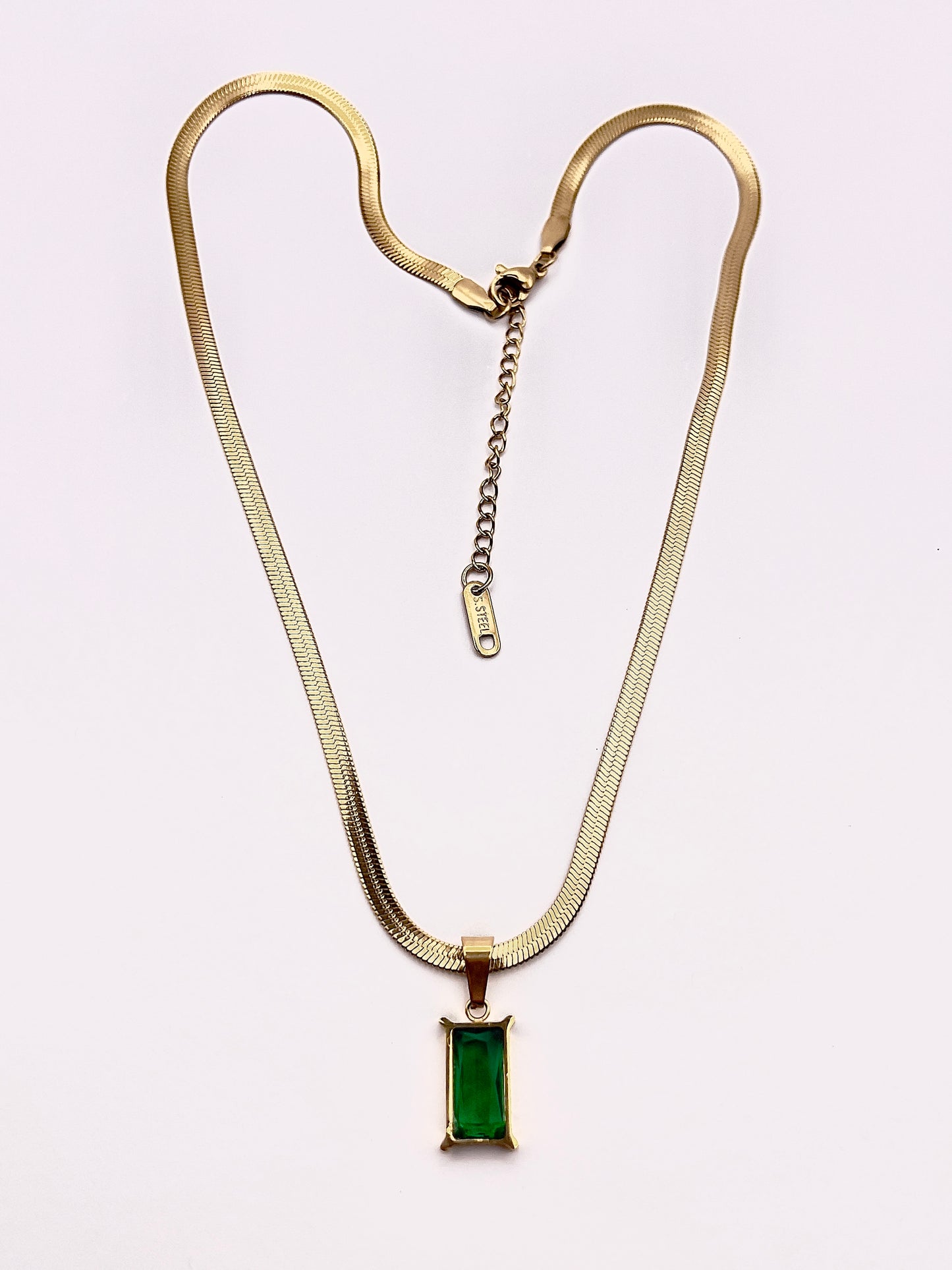 Full view of Fthi, A distinguished flowing gold plated herringbone necklace complimented with an emerald green zircon.