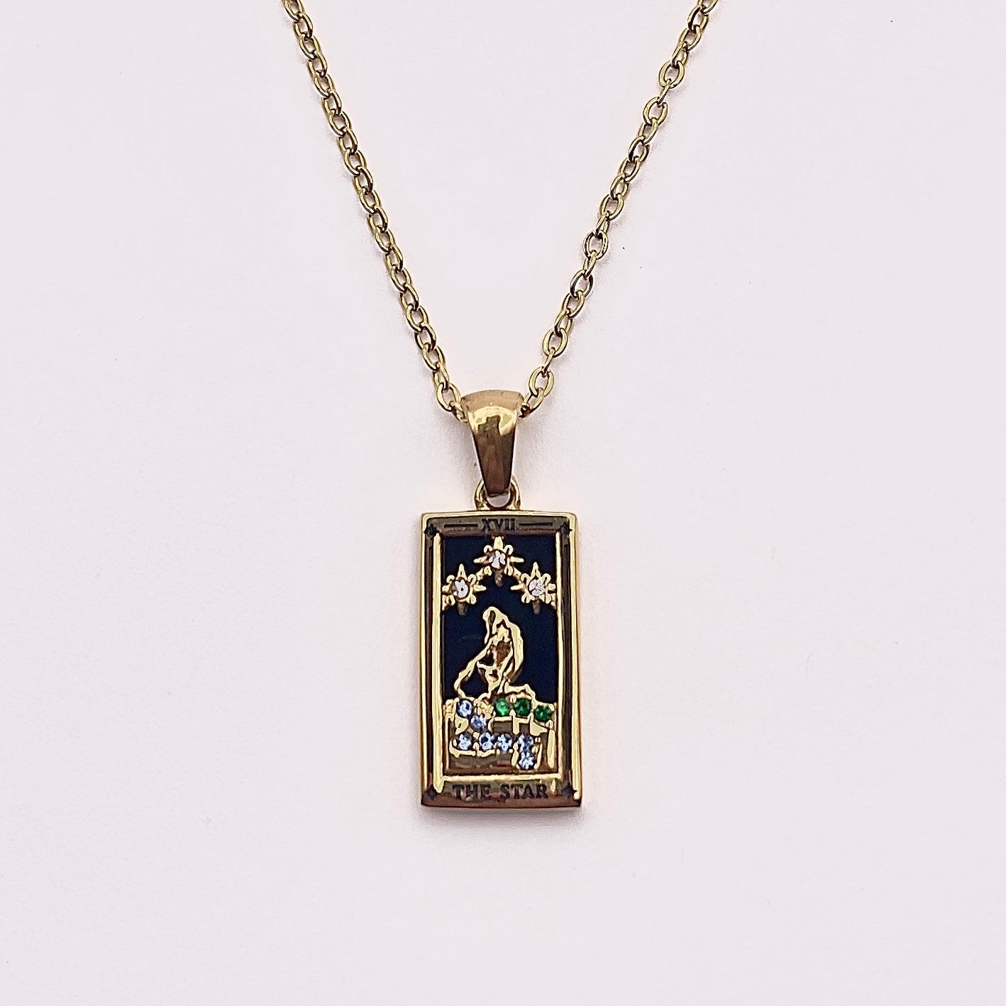 Front view of an enchanting gold plated necklace perfected with a rectangular tarot card, the Star (-XVII-), sculpted with stunning gold plated artistry, detailed with white and green zircons, and black stone backed.