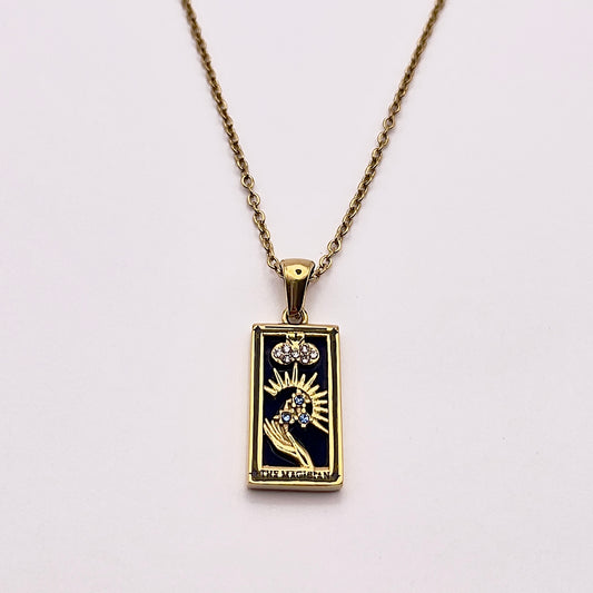 Front view of an enchanting gold plated necklace perfected with a rectangular tarot card, the Magician (-I-), sculpted with stunning gold plated artistry, detailed with white and blue zircons, and black stone backed.