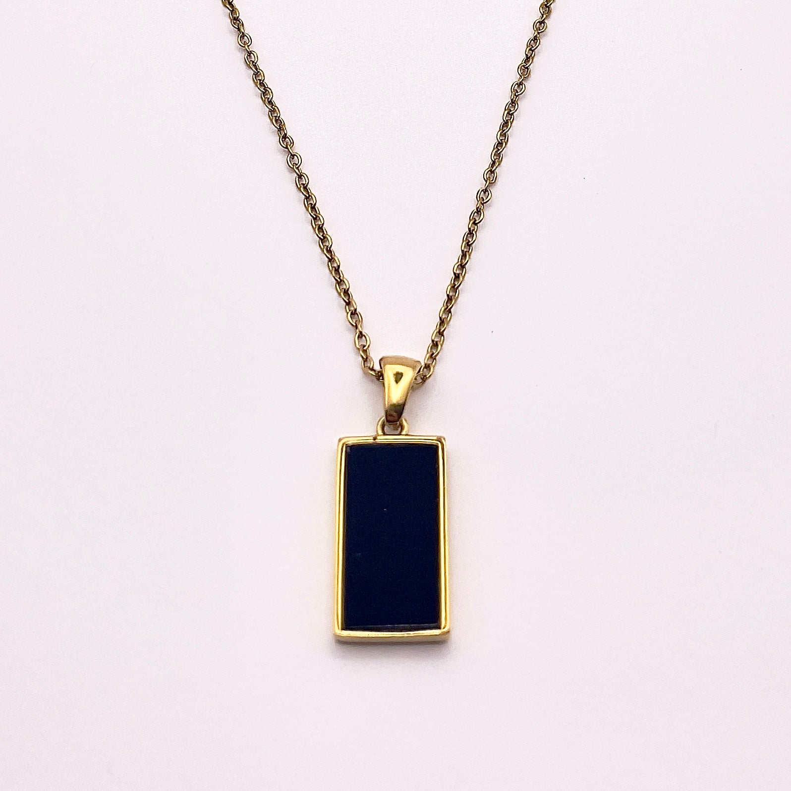 Back view of an enchanting gold plated necklace perfected with a rectangular tarot card, the World (-XXI-), sculpted with stunning gold plated artistry, detailed with white and blue zircons, white enamel, and black stone backed.