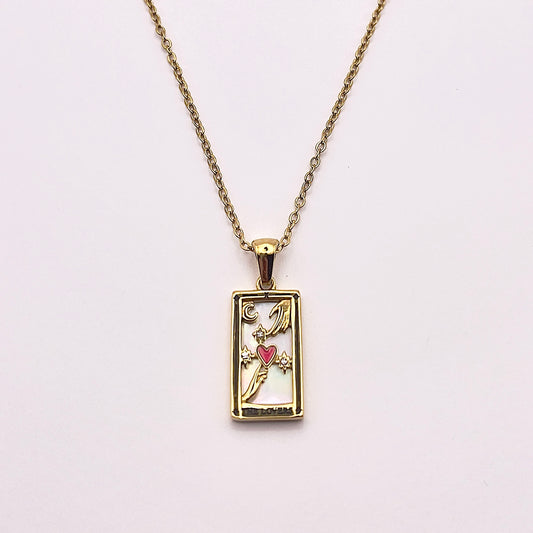 Front view of an enchanting gold plated necklace perfected with a rectangular tarot card, the Lovers (-X-), sculpted with stunning gold plated artistry, detailed with white zircons and red enamel, and white pearl colored stone backed.