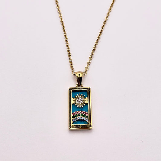 Front view of an enchanting gold plated necklace perfected with a rectangular tarot card, the Sun (-XIX-), sculpted with stunning gold plated artistry, detailed with pink, green, and white zircons, and blue lapis lazuli replica stone backed.