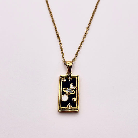 Front view of an enchanting gold plated necklace perfected with a rectangular tarot card, the World (-XXI-), sculpted with stunning gold plated artistry, detailed with white and blue zircons, white enamel, and black stone backed.