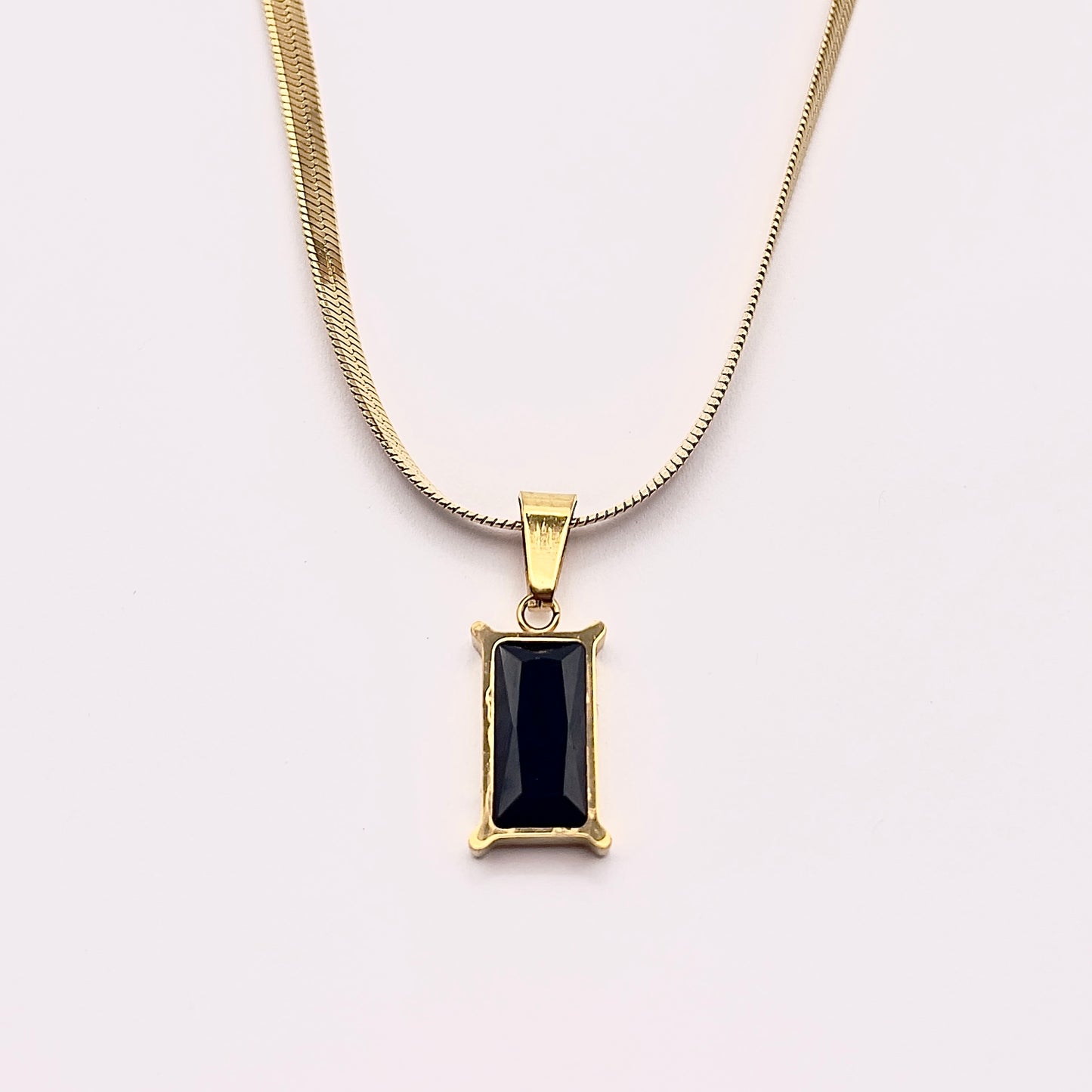 Close up view of Fthi, a distinguished flowing gold plated herringbone necklace complimented with an obsidian black zircon.