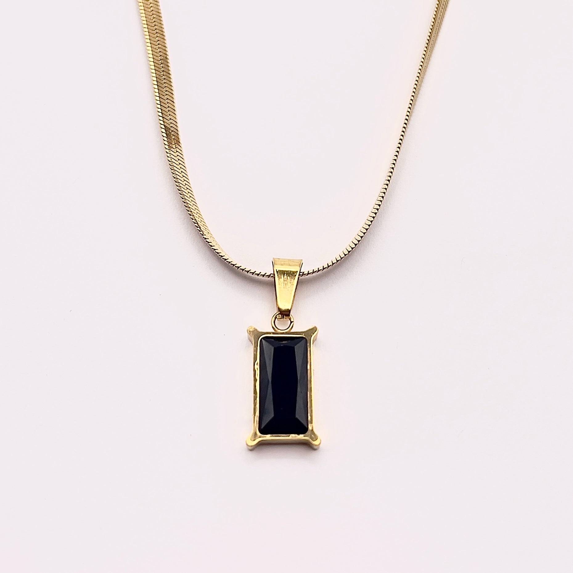 Close up view of Fthi, a distinguished flowing gold plated herringbone necklace complimented with an obsidian black zircon.