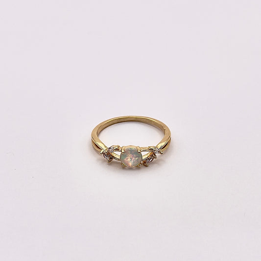 Front view of Alio, a charming warm replica opal ring nested in an elven yellow gold plated band accented with zircon petals.