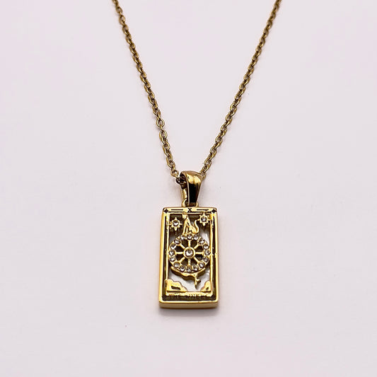 Front view of an enchanting gold plated necklace perfected with a rectangular tarot card, the Wheel (-X-), sculpted with stunning gold plated artistry, detailed with white zircons, and white pearl colored stone backed.