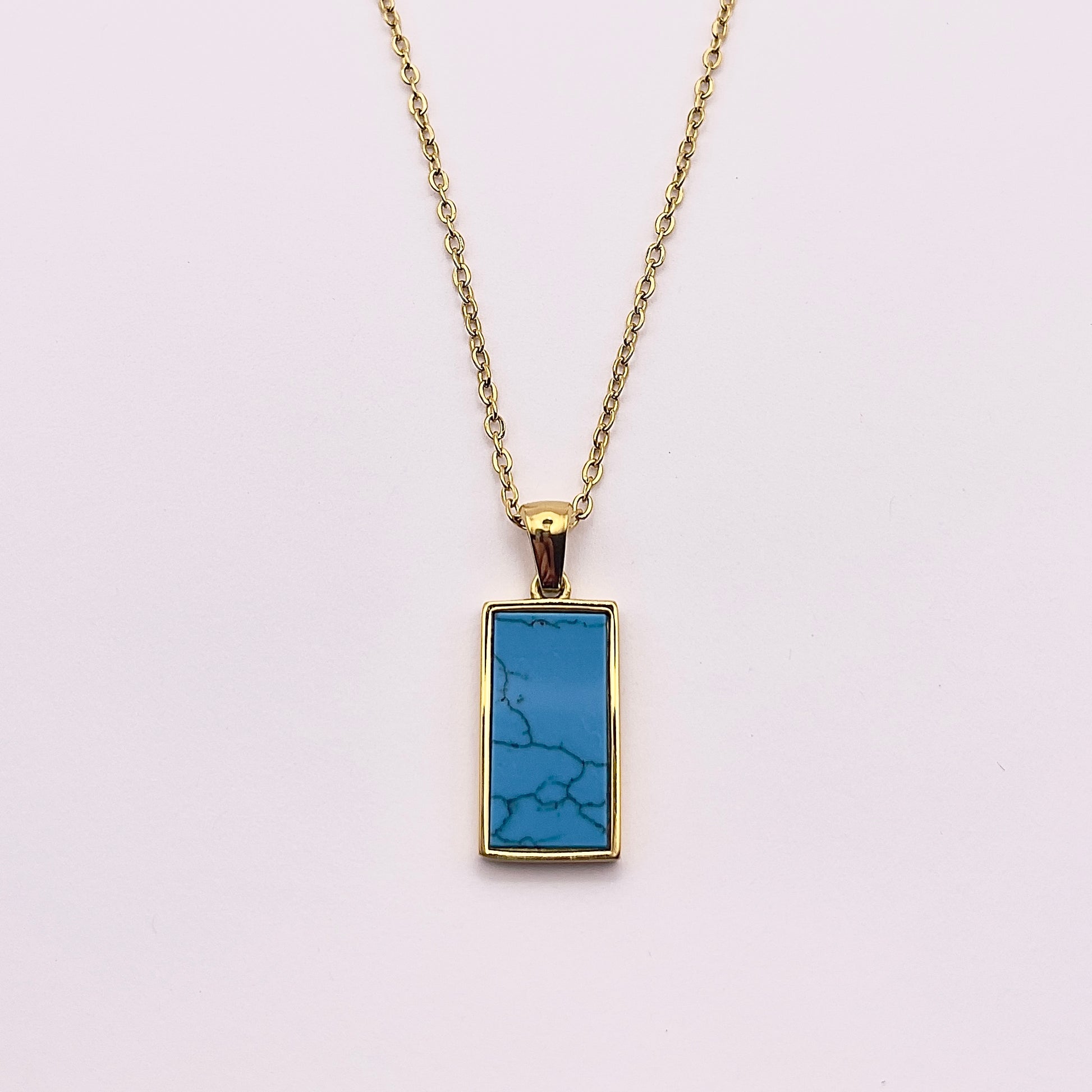 Back view of an enchanting gold plated necklace perfected with a rectangular tarot card, the Sun (-XIX-), sculpted with stunning gold plated artistry, detailed with pink, green, and white zircons, and blue lapis lazuli replica stone backed.