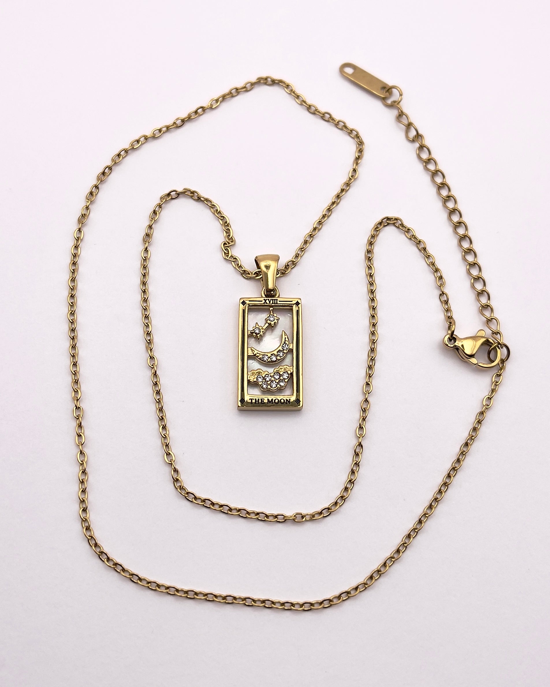 Full front view of An enchanting gold plated necklace perfected with a rectangular tarot card, the Moon (-XVIII-), sculpted with stunning gold plated artistry, detailed with white zircons, and white pearl colored stone backed.