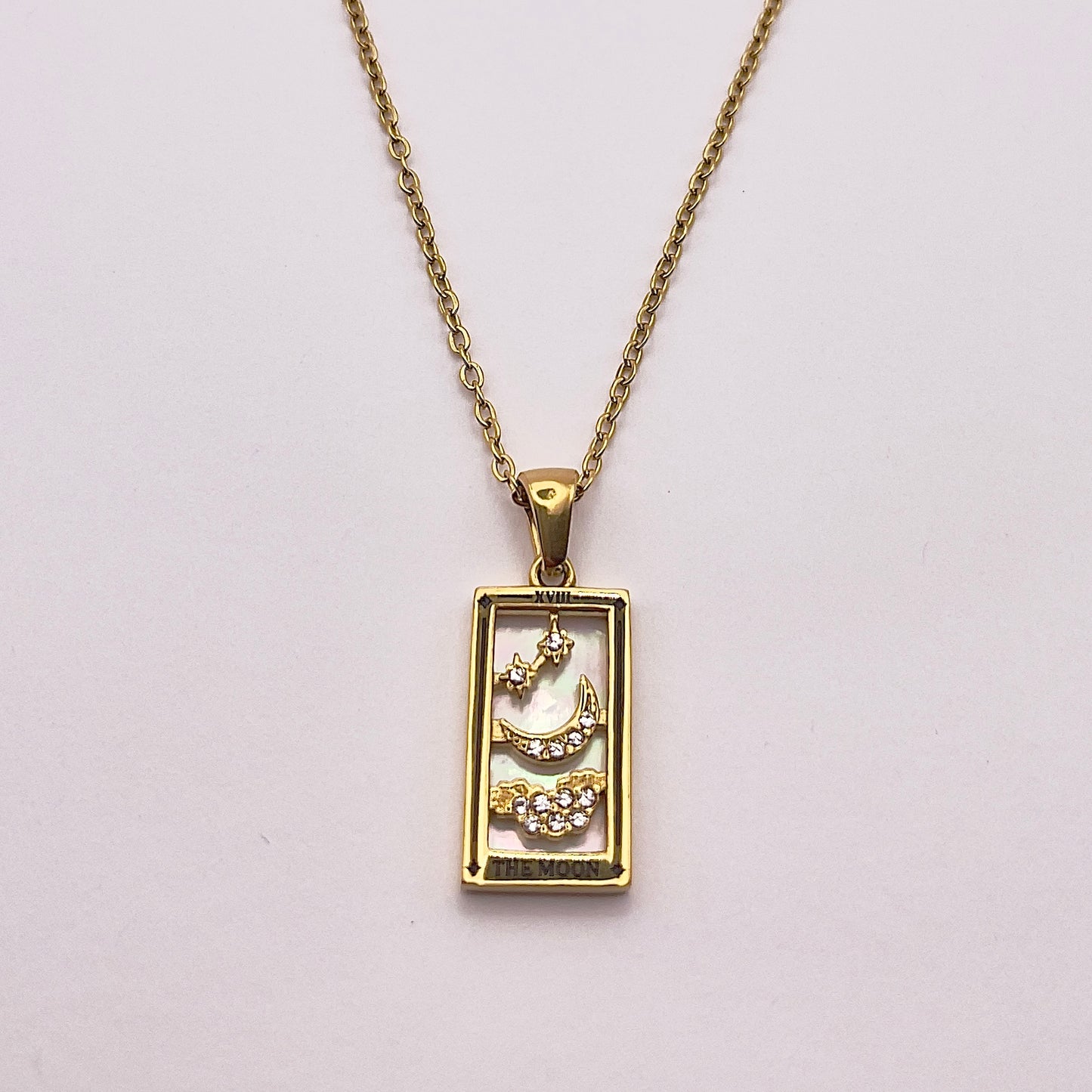 Front view of An enchanting gold plated necklace perfected with a rectangular tarot card, the Moon (-XVIII-), sculpted with stunning gold plated artistry, detailed with white zircons, and white pearl colored stone backed.