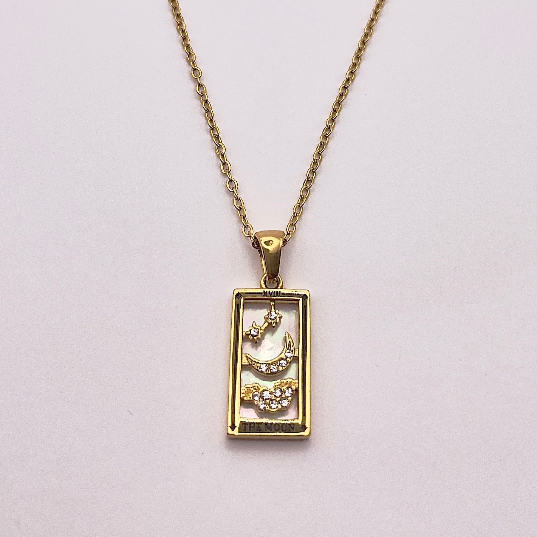 Front view of An enchanting gold plated necklace perfected with a rectangular tarot card, the Moon (-XVIII-), sculpted with stunning gold plated artistry, detailed with white zircons, and white pearl colored stone backed.