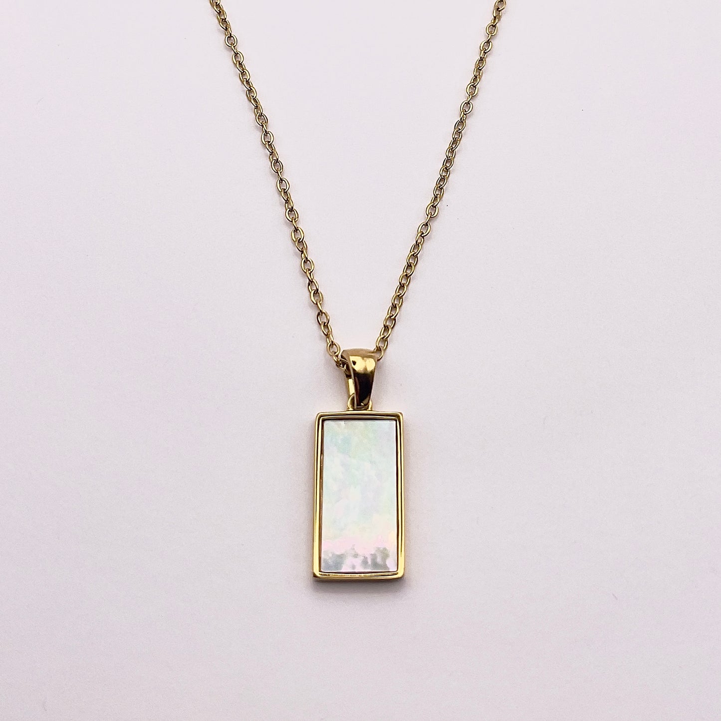 Back view of an enchanting gold plated necklace perfected with a rectangular tarot card, the Lovers (-X-), sculpted with stunning gold plated artistry, detailed with white zircons and red enamel, and white pearl colored stone backed.